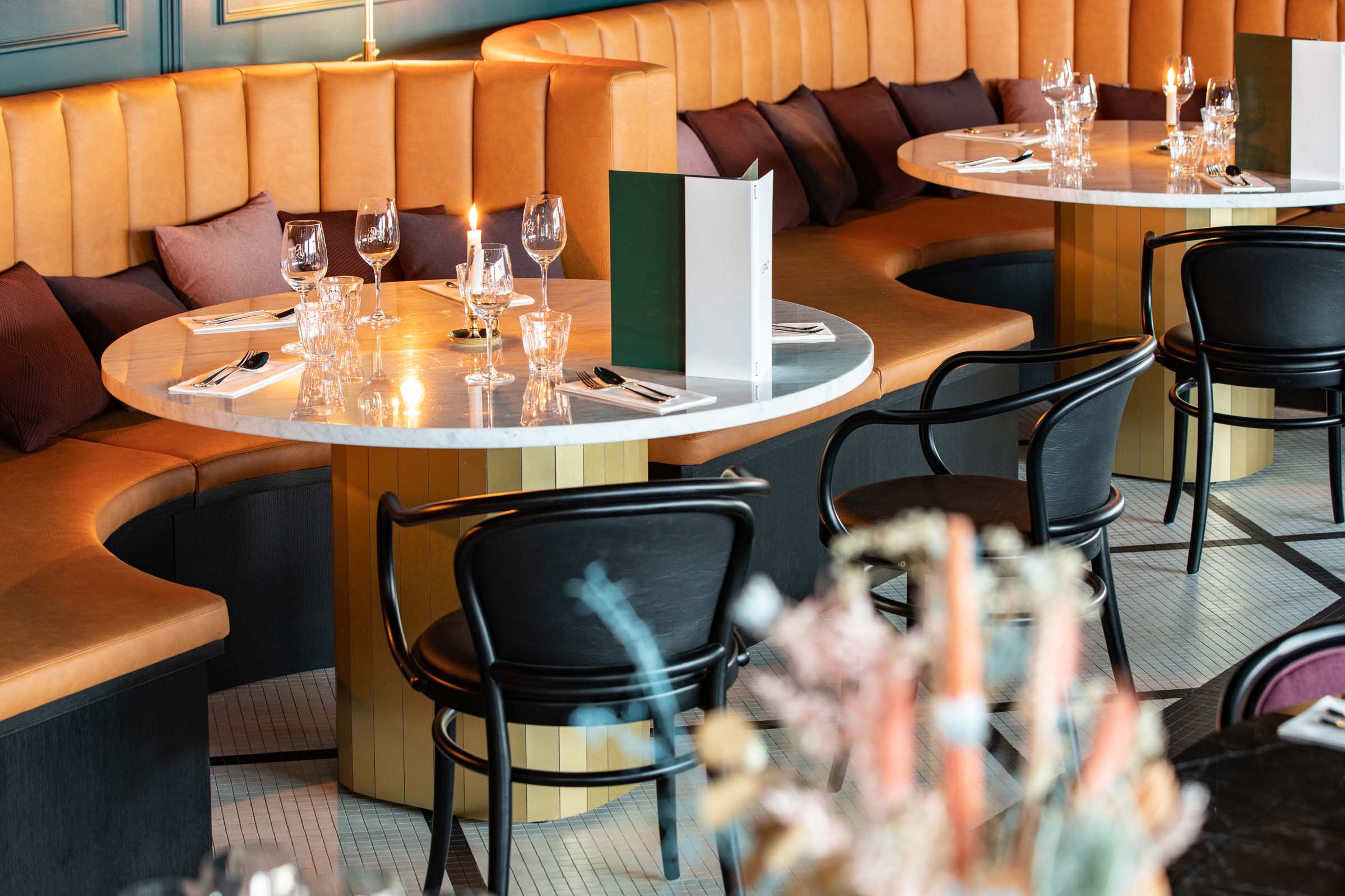 Ravintola Vespino, terracotan väriset kaarevat sohvapenkit ja marmorikantiset pyöreät ruokapöydät.