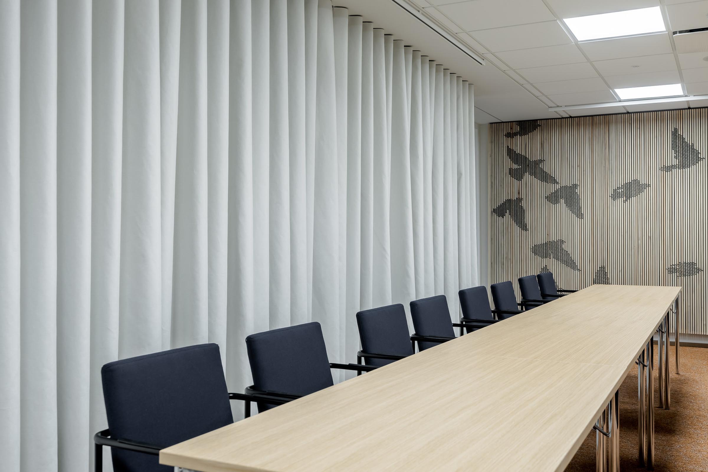 Varsinais-Suomen liiton toimisto, graafinen lintuteos puurimaseinällä, edessä pöytä ja tuolirivi.